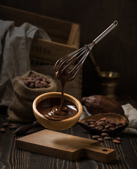 Dark still life with melted chocolate in wooden bowl
