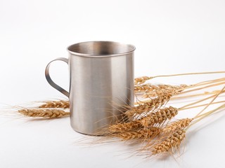 wheat spikelets and metal mug on white background