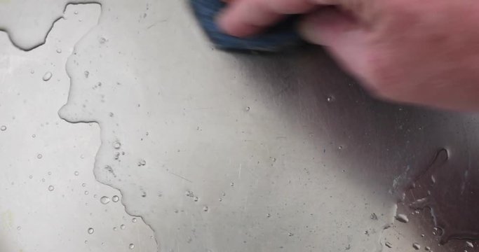 Close video of using a stainless steel scouring pad to clean a stainless steel pan..