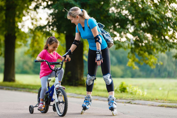 A young mother roller skating. her Daughter riding a bicycle