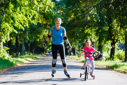 A young mother roller skating. her Daughter riding a bicycle