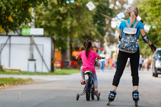 A young mother roller skating. her Daughter riding a bicycle