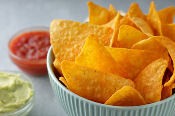 Bowl of nachos close-up with dip sauces on gray stone background.