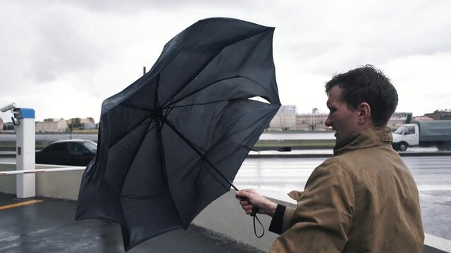 Man in jacket with umbrella standing outdoors. The gust of wind pulls umbrella out of hand
