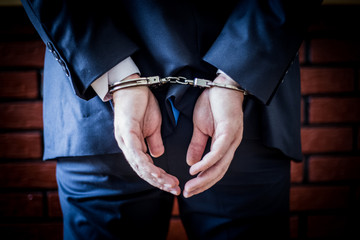 Businessman with hands on the back and handcuffs on. Arrested for corruption and crime in business...