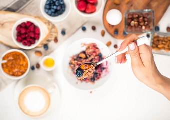 Top view showing hands eating porridge with honey nuts, blueberries on white wooden table selective focus, blurred background Good morning - healthy breakfast background