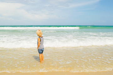 A thoughtful blond boy (child) staying in water at a sea shore (beach), Nha Trang, Vietnam