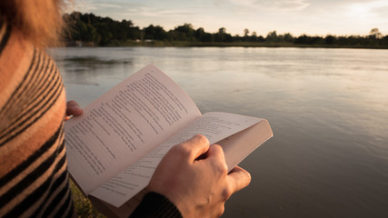 Close up hand of young woman reading the book at riverside in the evening.