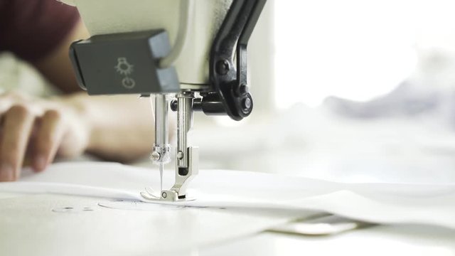Close up of an unrecognizable semstress hands sewing a white shirt at a factory. She is using a sewing machine. Locked down real time close up shot