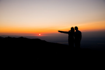 Couple watching sunset over the mountains. Holding each other. Romantic scenery. Friendship.