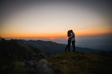Fototapeta premium Couple watching sunset over the mountains. Holding each other. Romantic scenery. Friendship.