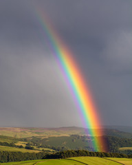 Colourful rainbow shining down on valley with dark moody clouds in background.