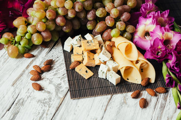 Assortment of cheeses with nuts and grapes on a white wooden background