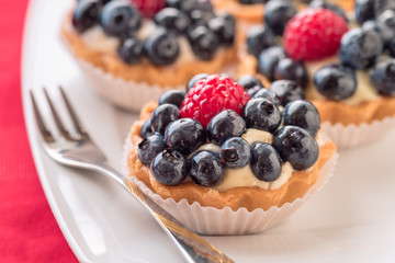Tartlets with blueberries and raspberry on white plate.