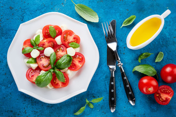 Salad caprese. Cheese mozzarella, tomatoes, olive oil and basil herb leaves on concrete background. Healthy eating. Top view