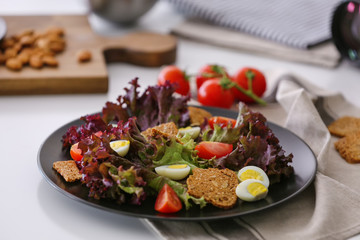 Salad with cherry tomatoes and quail eggs served on black plate, closeup