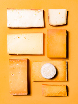 Various Hard Cheeses Arranged Neatly on Yellow Orange Background