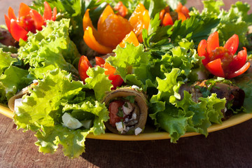 eggplant rolls and lettuce leaves decorated with flowers cut from cherry tomatoes on wooden background side view