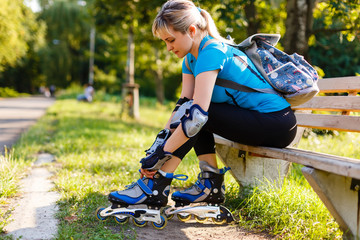 Athletic woman sitting on a bench in a park and putting on inline skates. Close up. Sport lifestyle.