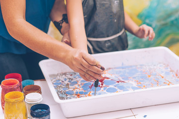 The master teaches the girl the technique of ebru. Hands close up