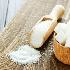 Wooden scoop and bowl with sugar on table, closeup