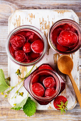 Homemade strawberry jam with whole berries in glass jars on wooden table. Toned image. Copy space