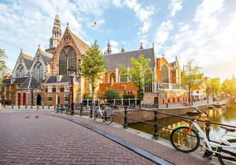 Fototapeta premium Poranny widok na kanał wodny ze Starym Kościołem podczas słonecznej pogody w mieście Amsterdam