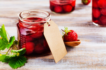 Homemade strawberry jam with whole berries in glass jars on wooden table. Toned image. Copy space