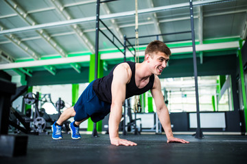 Fototapeta na wymiar Confident muscled young man wearing sport wear and doing plank position while exercising on the gym interior