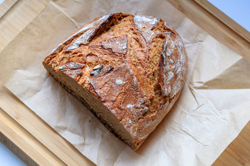 A fresh, crunchy, delicious rye bread on a wrinkled paper and a wooden chopping board