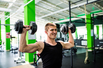 very power athletic man , execute exercise with dumbbells in gym