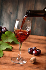 Pour red wine into the glass - wood background - closeup