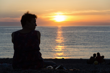 Silhouette of young woman sitting on the beach, watching the sunset