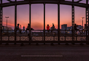 Sonnenuntergang in München an der Hackerbrücke mit sitzenden Personen vor dem Abendrot