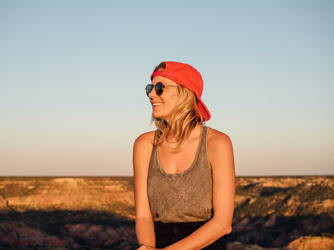 Young woman smiling in outdoor setting while wearing  sunglasses and backwards cap