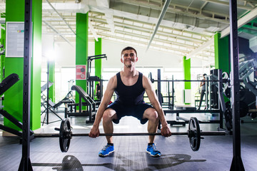 Close up of young muscular man lifting weights over gym background