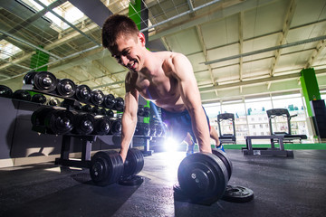 Strong, handsome man doing push-ups on dumbbells in a gym as bodybuilding exercise, training his...
