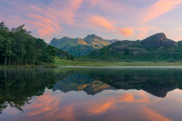 Fototapeta premium Lustrzane odbicia w jeziorze o wschodzie słońca z porannym światłem uderzającym w góry w Lake District.