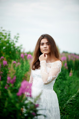 Fototapeta na wymiar Beautiful bride in bright lace dress. In a field with Ivan-tea. Natural beauty, minimal makeup and loose hair. A child of nature