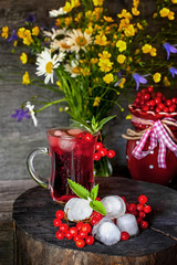 Fresh natural juice with ice and viburnum on a background of a beautiful bouquet of wildflowers.