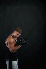 Fototapeta na wymiar Studio shot of muscular ripped young European bodybuilder dressed in sweatpants and black tank top exercising with dumbbells. Health, fitness, sports, bodybuilding and weightlifting concept