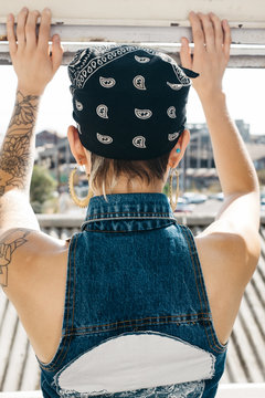 Tattooed woman in vest and bandana standing back