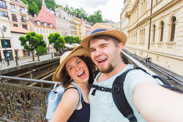 Fototapeta na wymiar Happy young couple in love takes selfie portrait in Karlovy Vary in Czech Republic. Pretty tourists make funny photos for travel blog in Europe.