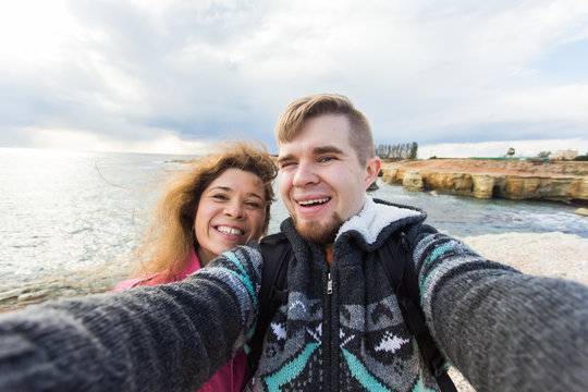 Happy traveling couple in love taking a selfie on phone at the beach on winter or autumn day. Pretty girl and her handsome boyfriend having fun, crazy emotional faces , laughing.