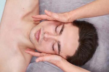 Fototapeta na wymiar Facial massage, young handsome man. Hands massaging face, top view. Health and beauty of skin.