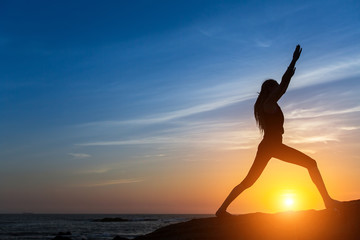 Silhouette woman doing fitness exercise on the sea beach during amazing sunset.