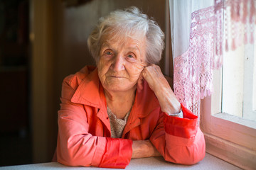 Elderly woman in red jacket sitting at the table in the house.