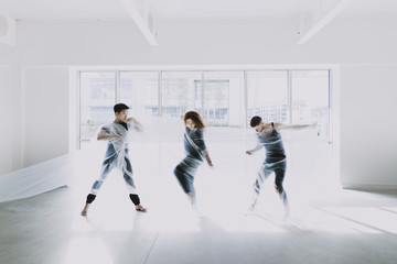 Three dancers tangled in cellophane, moving in front of a bright window