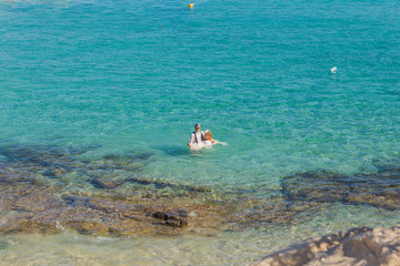 Top view of happy couple swims after wedding in turquoise sea. Romantic newly-married couple enjoying a summer vacation.