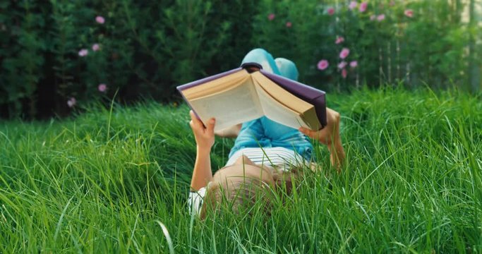 Girl reading book on the green grass. Dolly shot